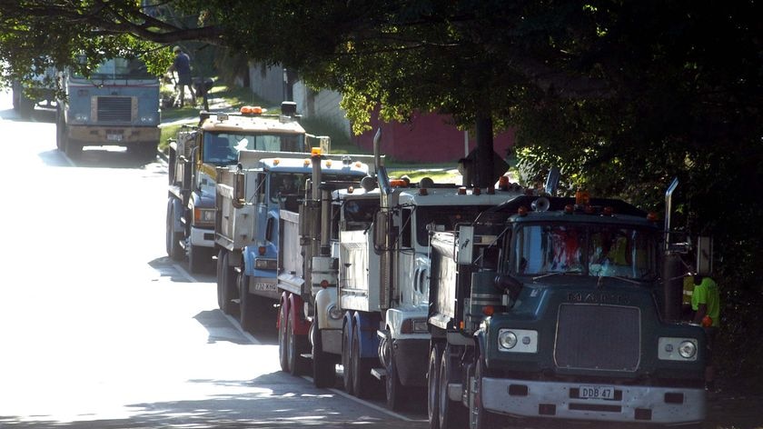A line of trucks wait to pick up loads of green refuse from houses at The Gap in Brisbane