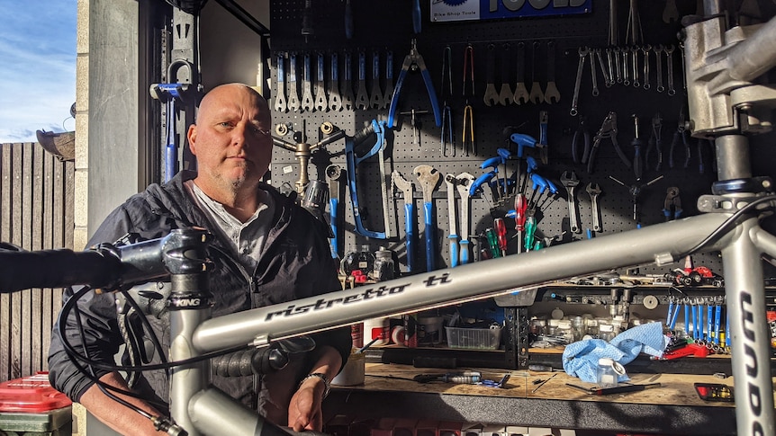 A man wearing a grey jumper standing behind a bike.