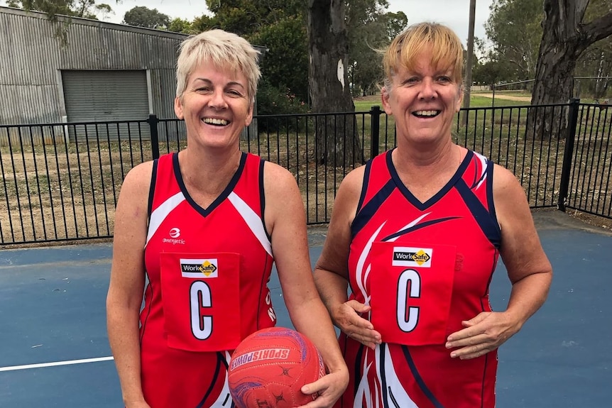 Wendy Sidebottom and a friend stand side by side on a netball court.