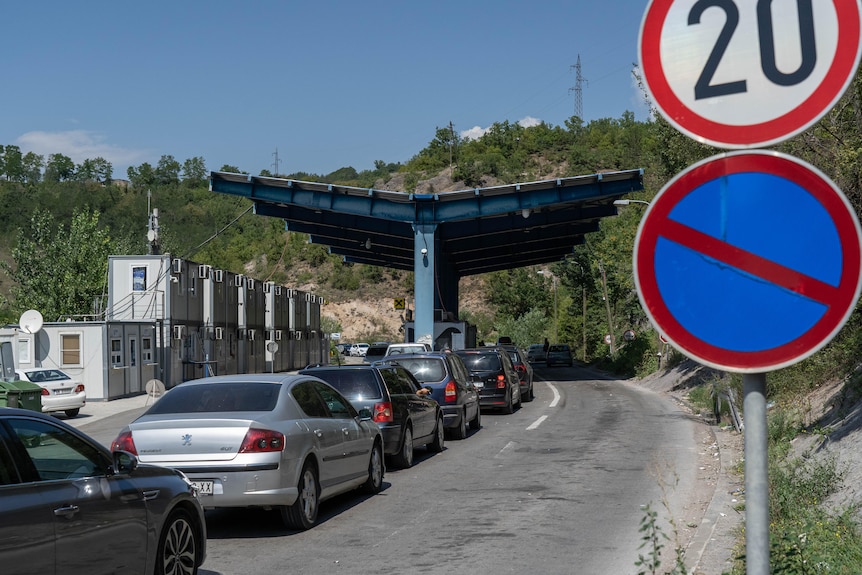 A queue of cars sit idle on a road near a border crossing.