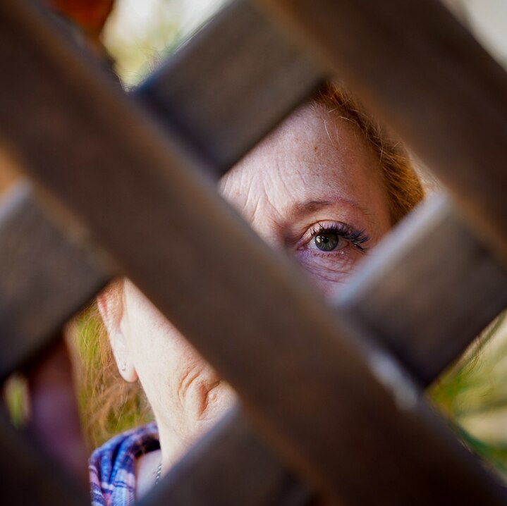 A woman peers through a fence, only her eye can be seen.