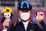 An Australian male competitor in the Tokyo Olympics equestrian competition wears a mask as he holds up his bronze medal.