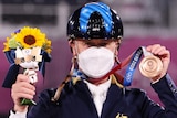 An Australian male competitor in the Tokyo Olympics equestrian competition wears a mask as he holds up his bronze medal.