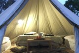 White glamping tent looking inside bed in background table and kettle in middle