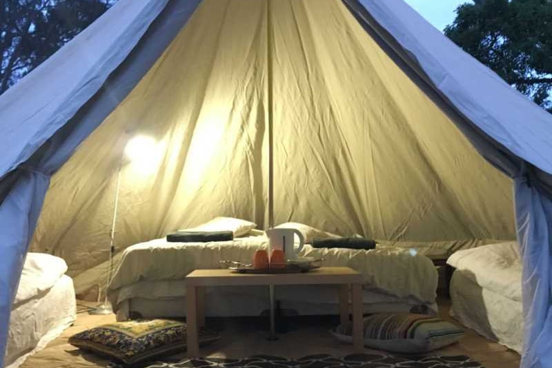 White glamping tent with a view of the bed in the background table and a kettle in the middle