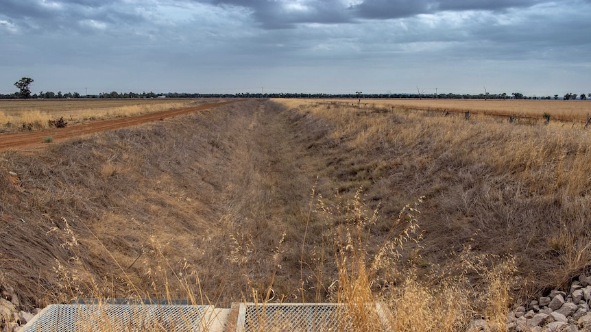 An empty irrigation channel in dry, brown fields.