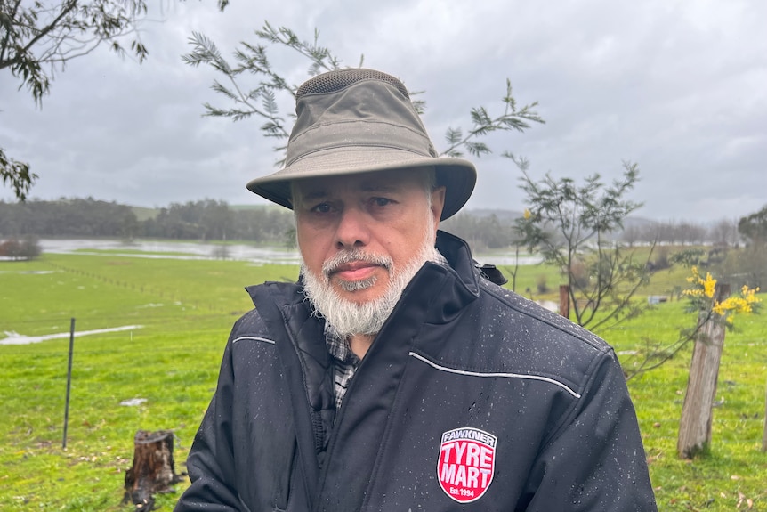 Uncle Andrew Gardiner appears thoughtful, dressed in a hat and rainjacket under grey skies in a green field.