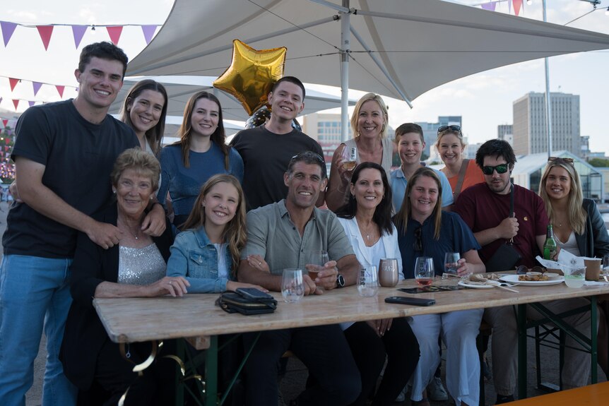 A group of people sitting at standing at an outdoor table at a Hobart venue, smiling at the camera. A star balloon behind them.