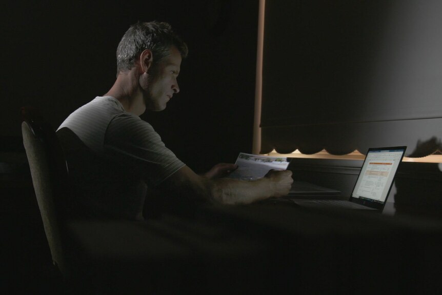A man sits in a dark room at a laptop computer