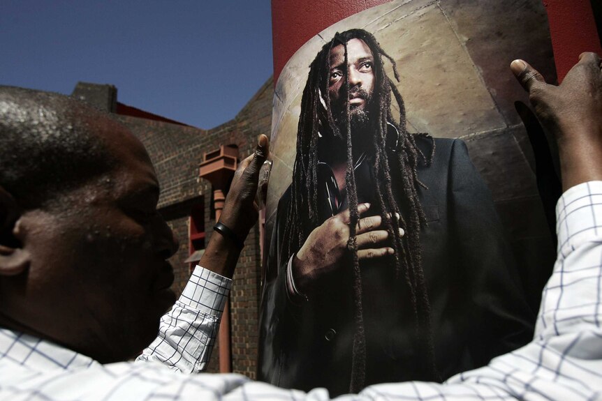 A man hangs a large poster of musician Lucky Dube.