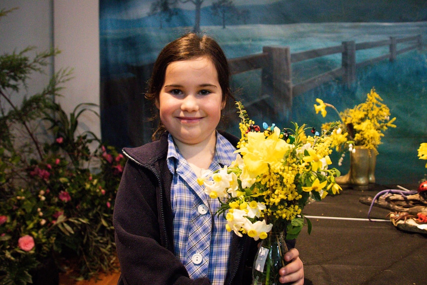 A girl holding a vase of yellow spring flowers smiles at the camera