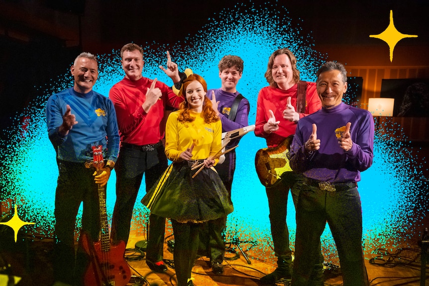 Photo of six Wiggles (including Emma as yellow wiggle) in skivvies at the triple j studio doing finger guns