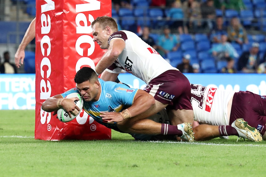 NRL player David Fifita is about to score, with two oppenents on his back trying to tackle him