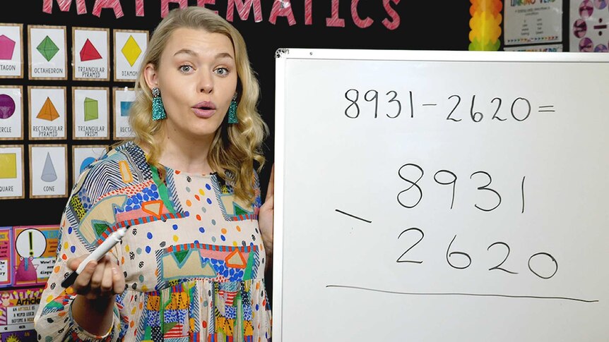 Female teacher stands in front of whiteboard showing equation