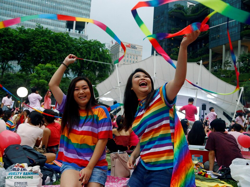 Two women wearing rainbow-coloured t-shirts while swinging rainbow flag strings.