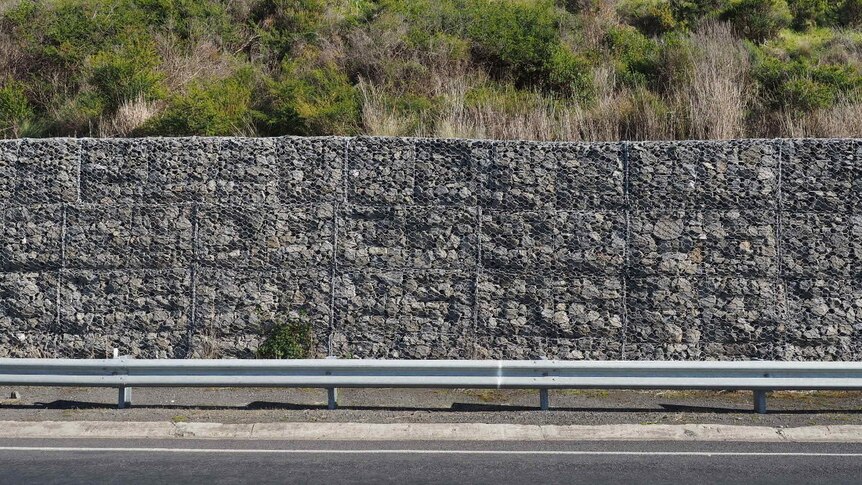 A 2m high wall made from grey rocks and held together with wire runs along a section of the hills beside the Great Ocean Road.