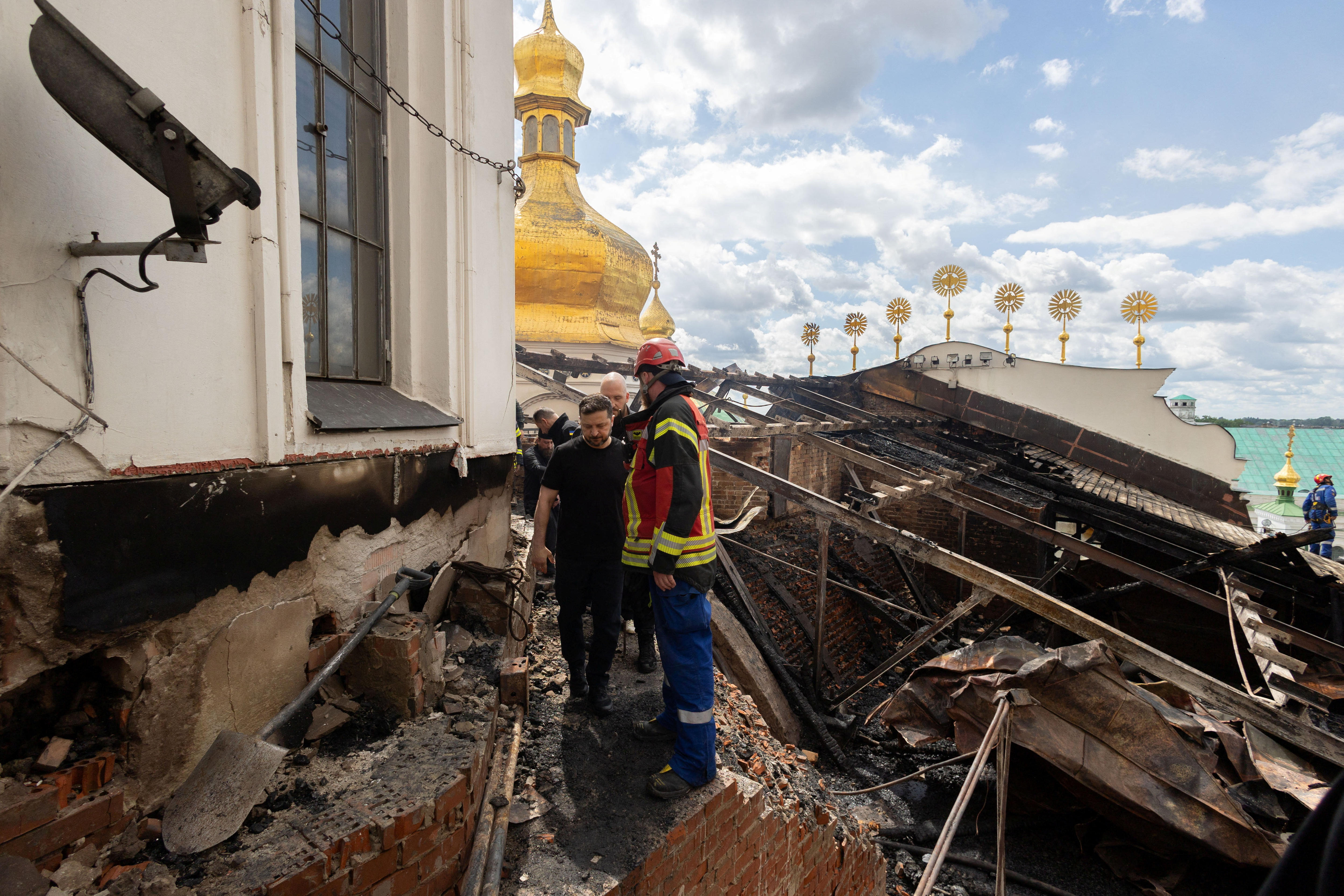 Ukraine's President Volodymyr Zelenskyy dressed in black walks through damage after cathedral fire. 
