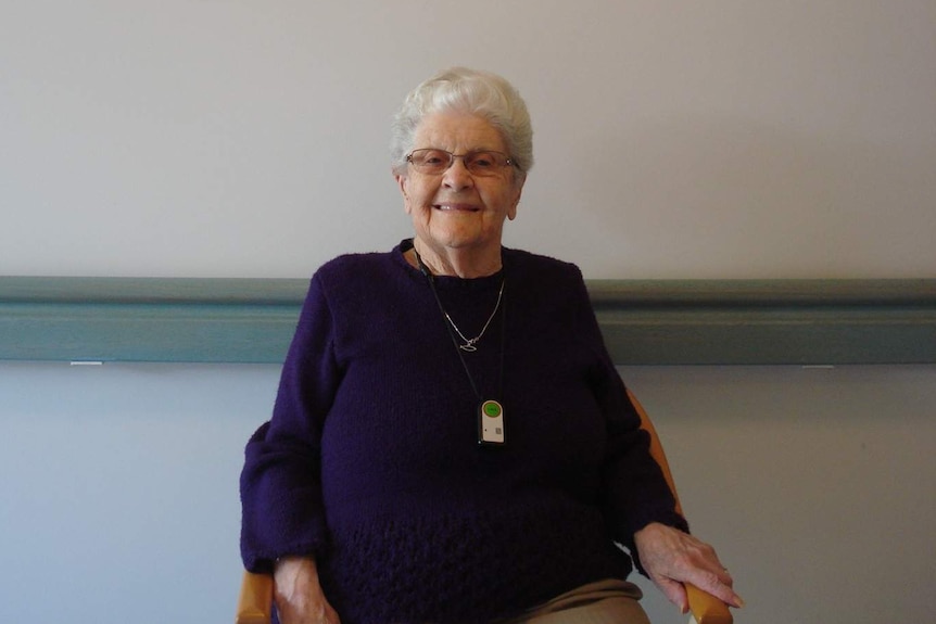 A lady sits in front of a wall in an aged care home.