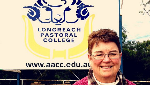 A lady standing in front of a sign for the Longreach Pastoral College.