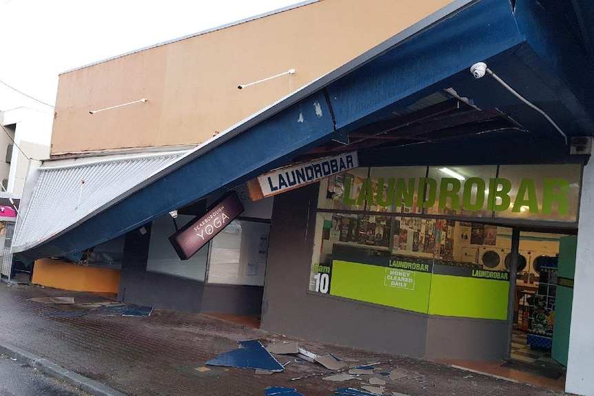 A row of businesses including a laundrobar and yoga studio with the street awning crashed to the floor.