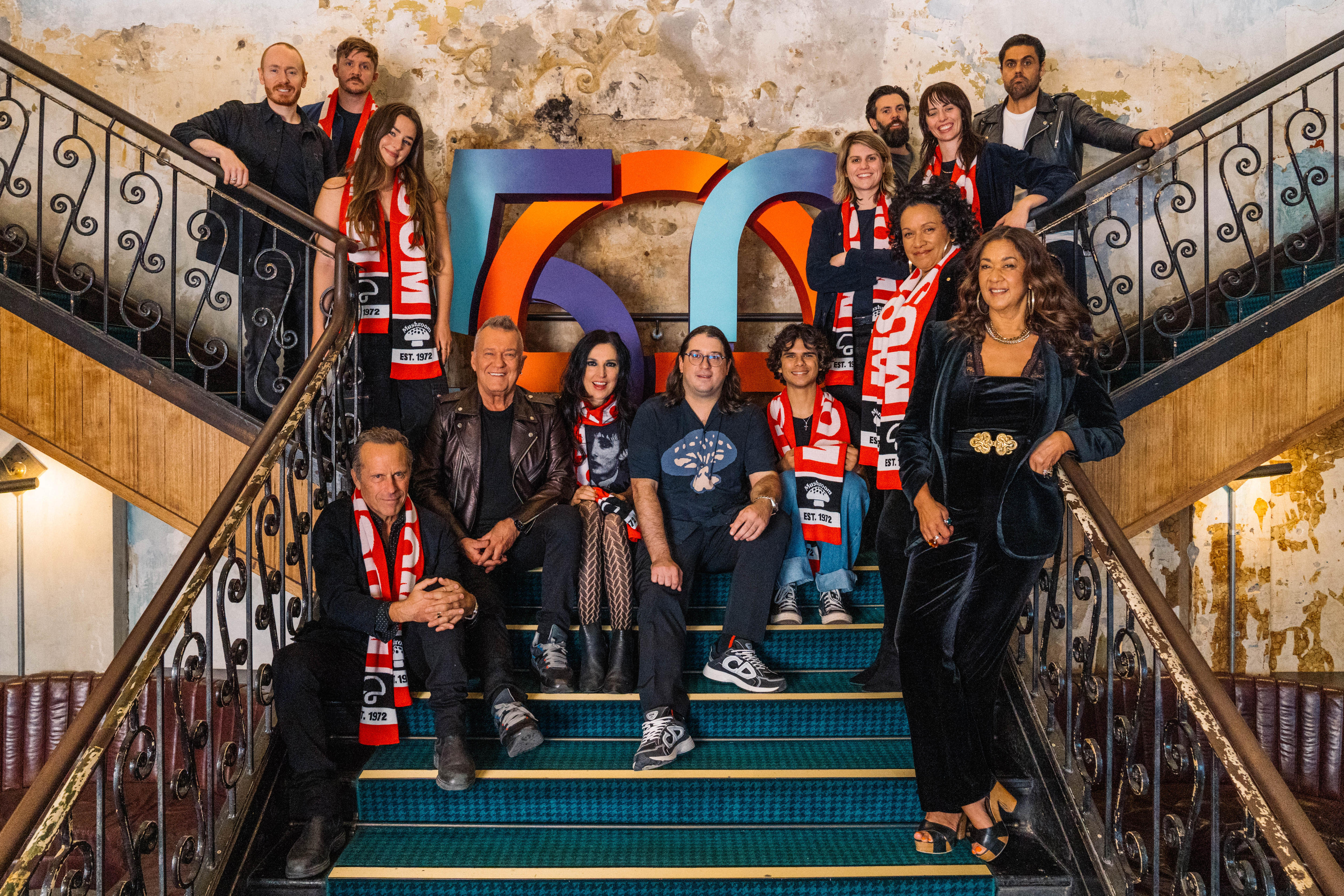 A group of musicians including Jimmy Barnes sit with Mushroom Group CEO Matt Gudinski on the stairs of a pub in Melbourne.