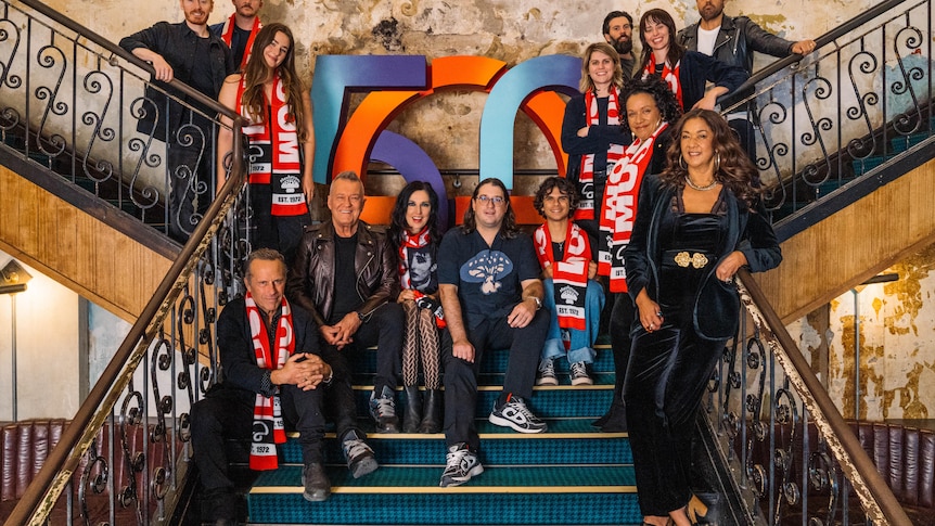 A group of musicians including Jimmy Barnes sit with Mushroom Group CEO Matt Gudinski on the stairs of a pub in Melbourne.