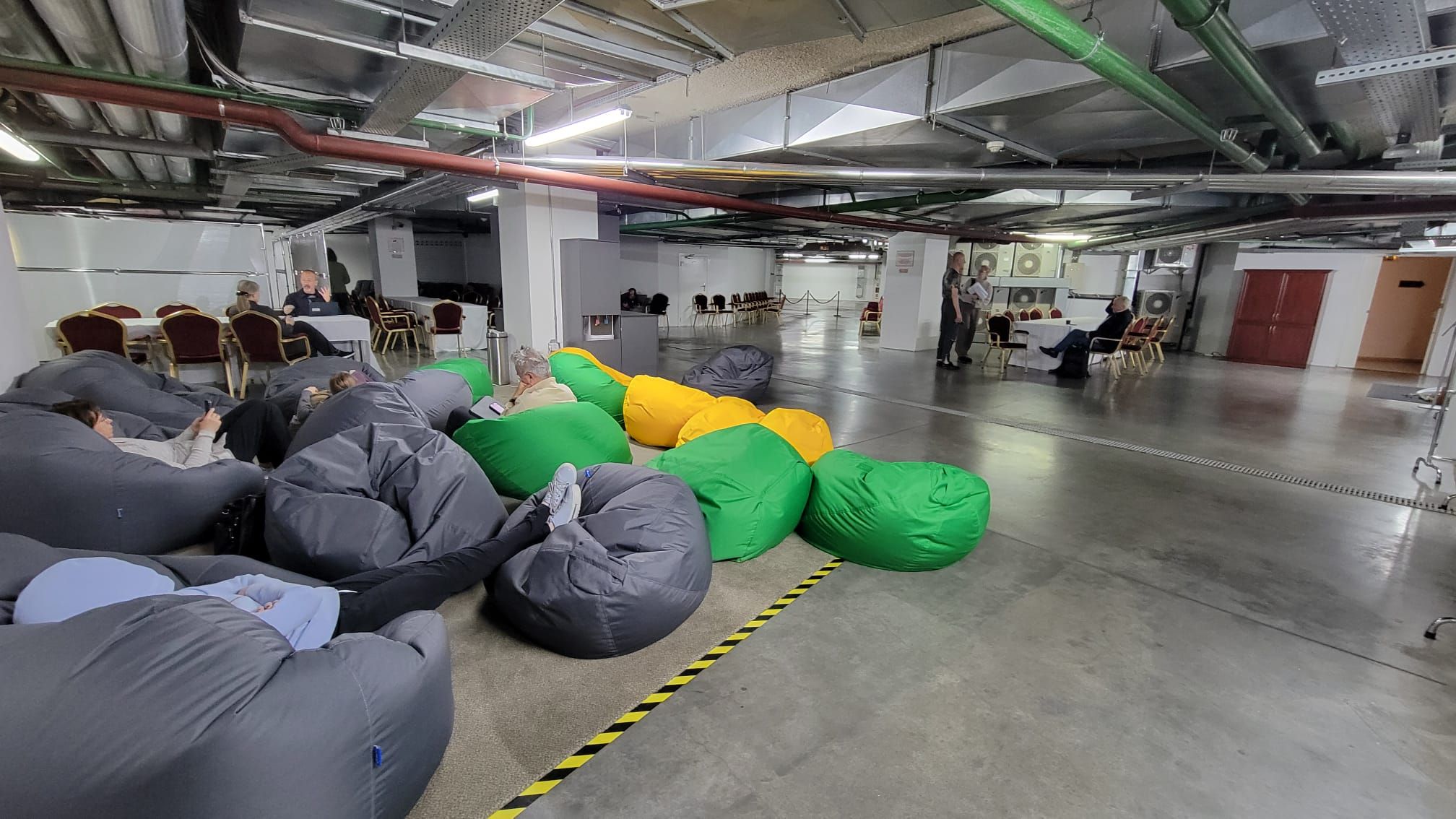 A sparse room with a concrete floor and bean bags with a table in the background. 