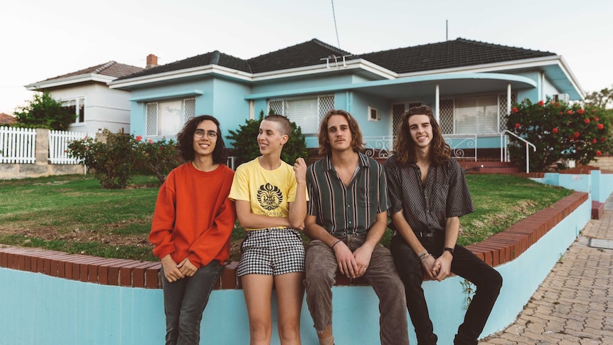 four band members sitting in front of a blue house