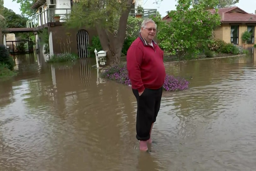 A man stands in floodwaters in front of houses.