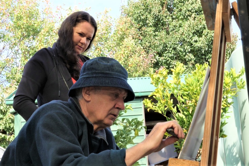 A woman watches her father paint