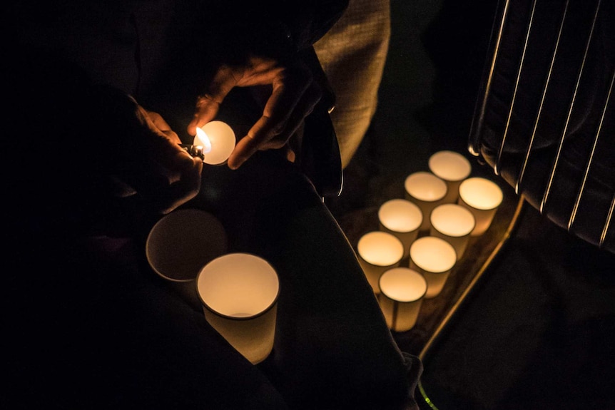 A resident lights candles as night falls over the camp