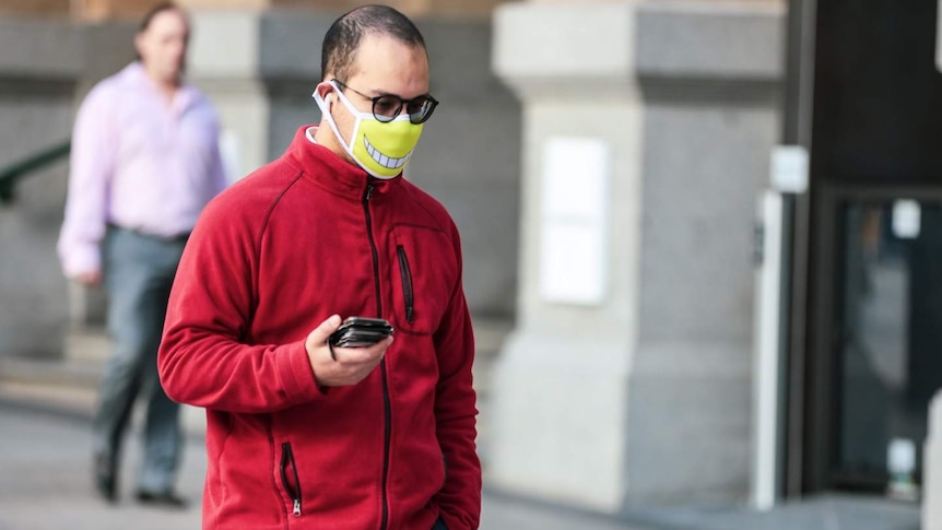 A man walking a city street wearing a face mask with a smile printed on the front