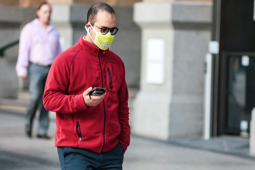 A man walking a city street wearing a face mask with a smile printed on the front