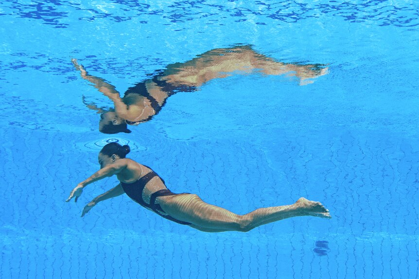 A woman floats unconscious near the surface of a pool.