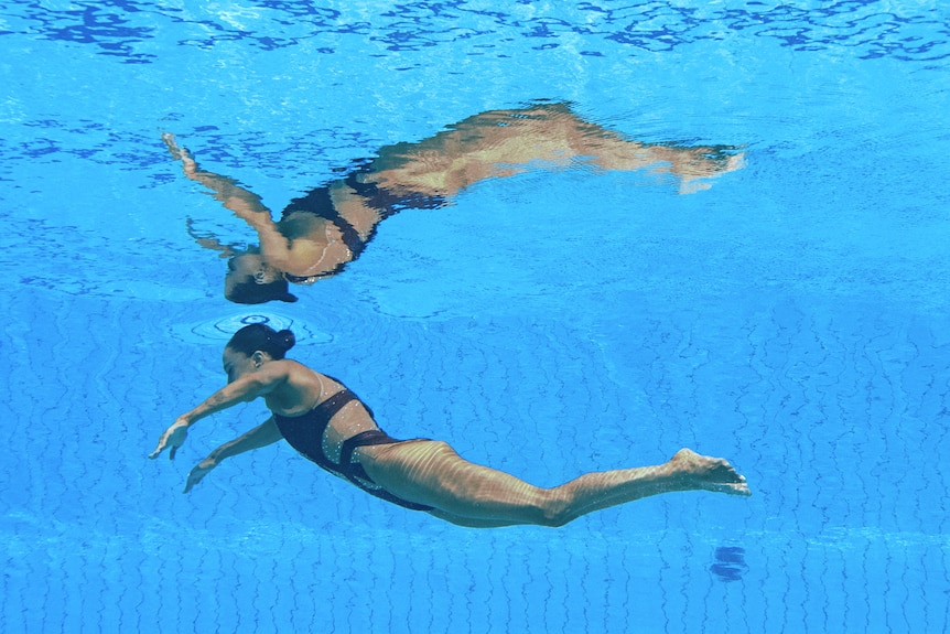 A woman floats unconscious near the surface of a pool.