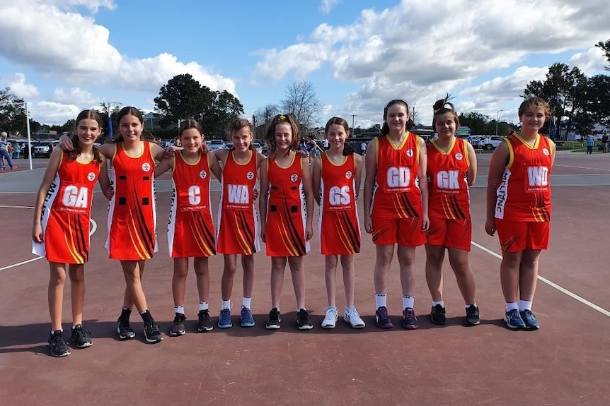 Junior netball team players wearing a mixture of netball dresses and shorts and singlets