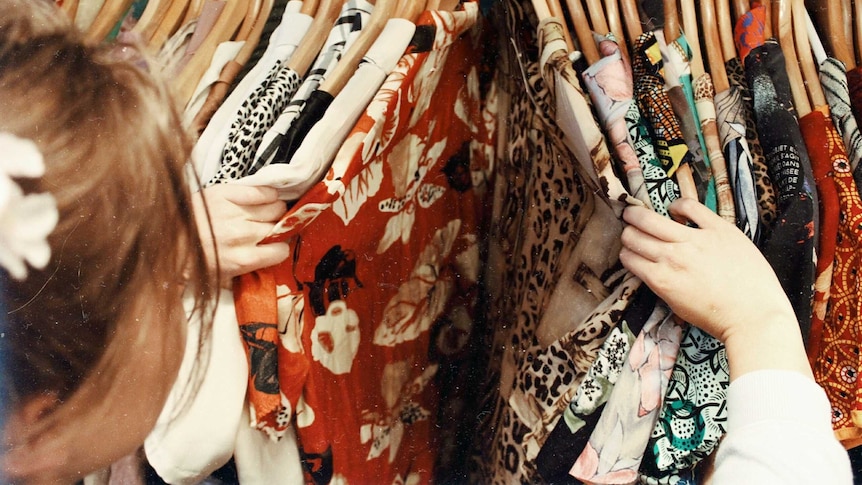 Close up of woman sorting through rack of button up shirt, representing the extra effort that ethical fashion finding requires.