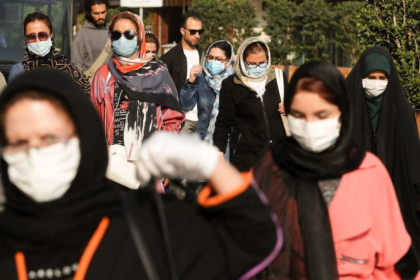 A group of women wearing masks and headscarves walk down a street