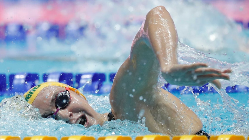 A female swimmer performs a freestyle strokes as she turns her head in the water to take a breath.