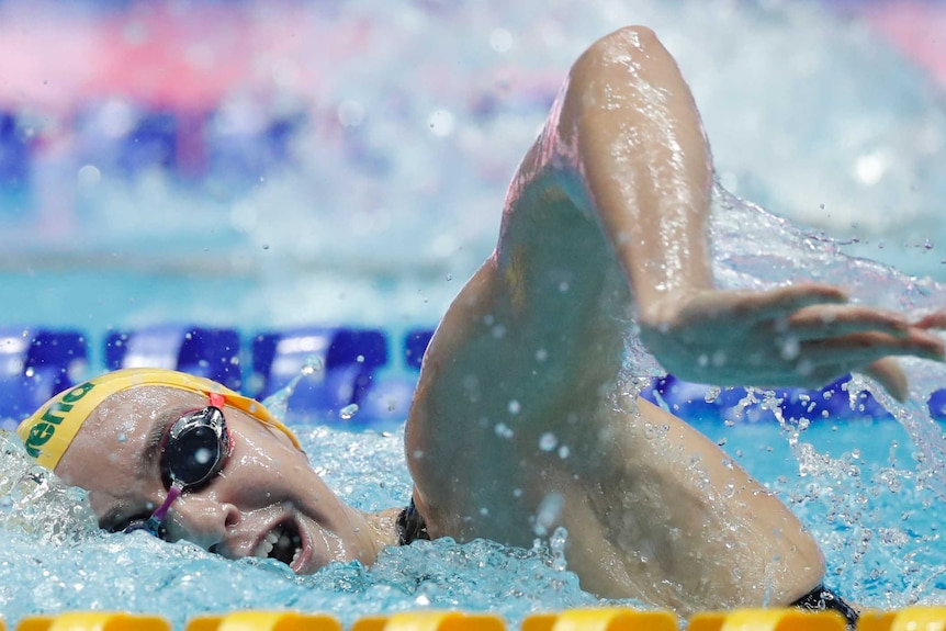 A female swimmer performs a freestyle strokes as she turns her head in the water to take a breath.