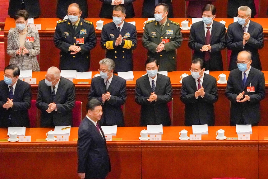 Xi Jinping passe devant une rangée de délégués chinois applaudissant masqués