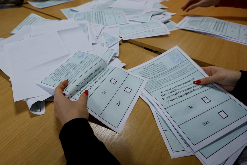 Ballots with cyrilic text are counted atop a wooden desk.