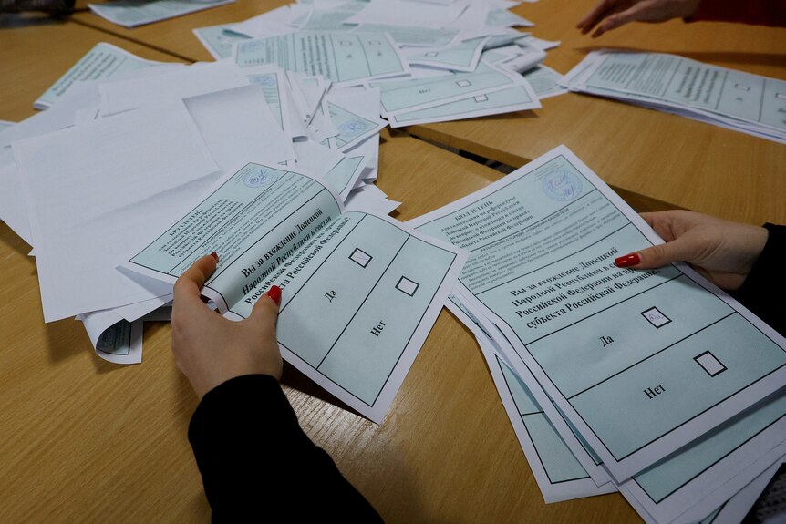 Ballots with cyrilic text are counted atop a wooden desk.