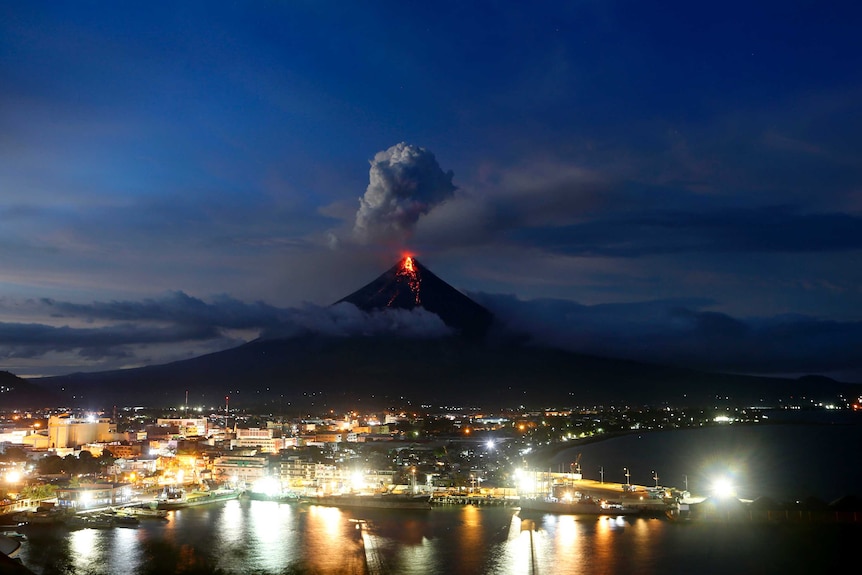 Glowing red lava erupts from Mayon volcano in the background as the sun sets behind Legazpi city