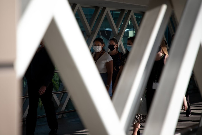 Mask wearing women viewed through a bridge's framework.