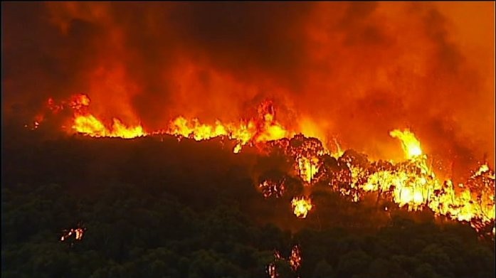 Flames from a huge bush fire tower over the blackened landscape turning the sky red.