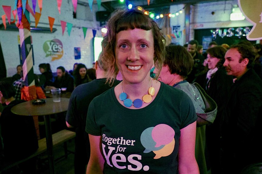 A young woman with a short fringe wears a green t-shirt that reads 'Together for Yes'.