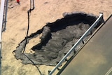 An aerial shot showing a hole full of black sludge in an area of sand.
