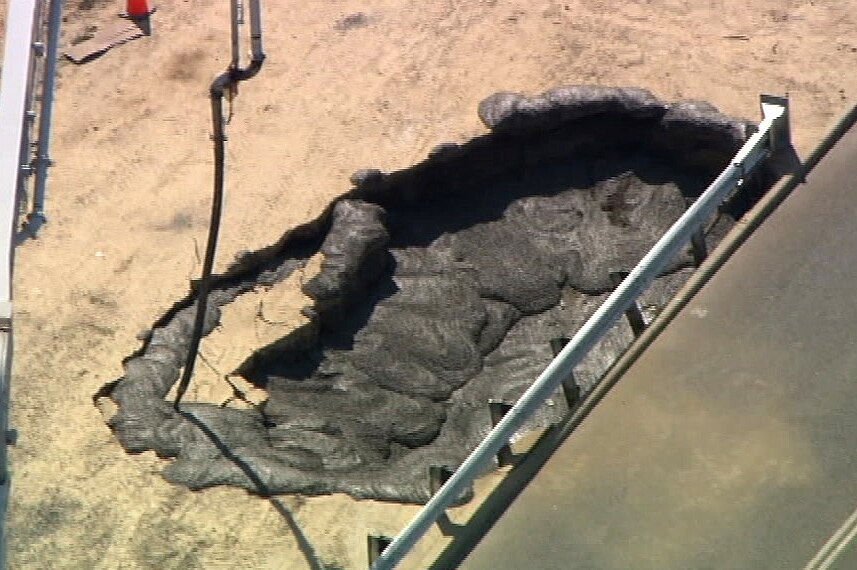 An aerial shot showing a hole full of black sludge in an area of sand.