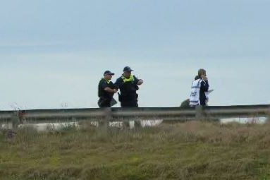 Police stand on a road at the top of an embankment.